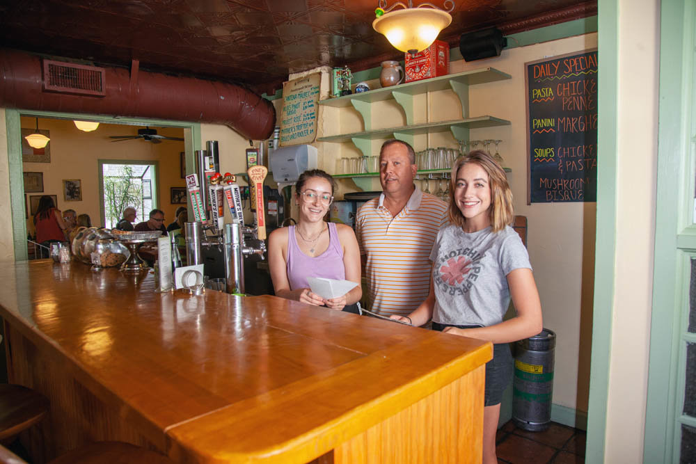 SEEING THE HIKE: Bambino’s Cafe co-owner Andy Faucett, center, says increases to the statewide minimum wage will cause his servers’ base pay to increase roughly 40 cents per year through 2023. That affects longtime employees like Sisilia Shaffer, left, and new hire Morgan Carleton, right.