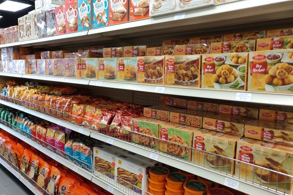 Food items including khari biscuits and dry kachori line the shelves at the new grocery.