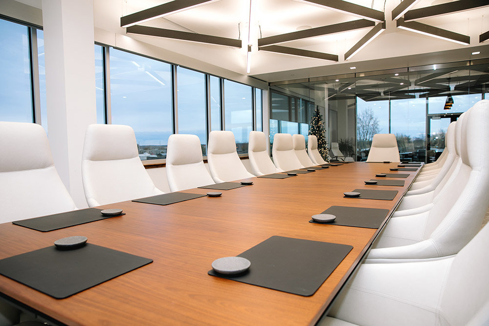 Plush white chairs neatly surround the top-floor conference room table. The space has an accordion glass wall that opens into an executive lounge and kitchen.