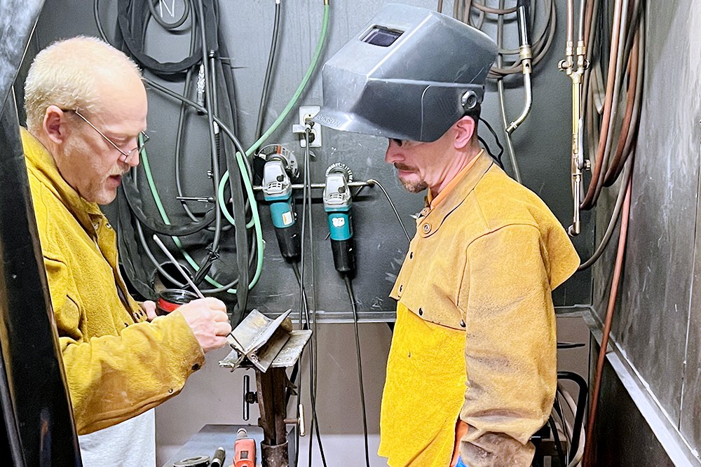 Andy McCarty, left, training coordinator for the Plumbers and Pipefitters Local 178 union, look over cohort participant Spencer Bowman's practice welding work.